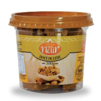 Pote plástico transparente de 300g do Doce de Leite em pedaços da Nhá Nair. O rótulo em tons de amarelo e bege destaca o nome da marca. No centro, uma imagem mostra pedacinhos quadrados de doce de leite em uma tigela.
