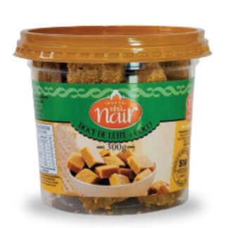 Pote plástico transparente de 300g do Doce de Leite com Coco em pedaços da Nhá Nair. O rótulo tem uma faixa principal em verde. No centro, uma imagem ilustra os cubos de doce de leite com flocos de coco, prontos para consumo.