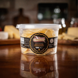 Pote transparente da marca Terra Canastra com lâminas douradas de provolone desidratado. O recipiente está sobre uma mesa de madeira, com fundo desfocado de cozinha.