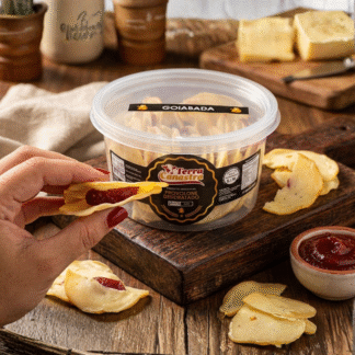 Pote transparente Terra Canastra com chips de provolone recheados de goiabada; uma mão exibe um chip de lado mostrando o recheio. Ao redor, tábua de madeira, queijo e potinho de goiabada.
